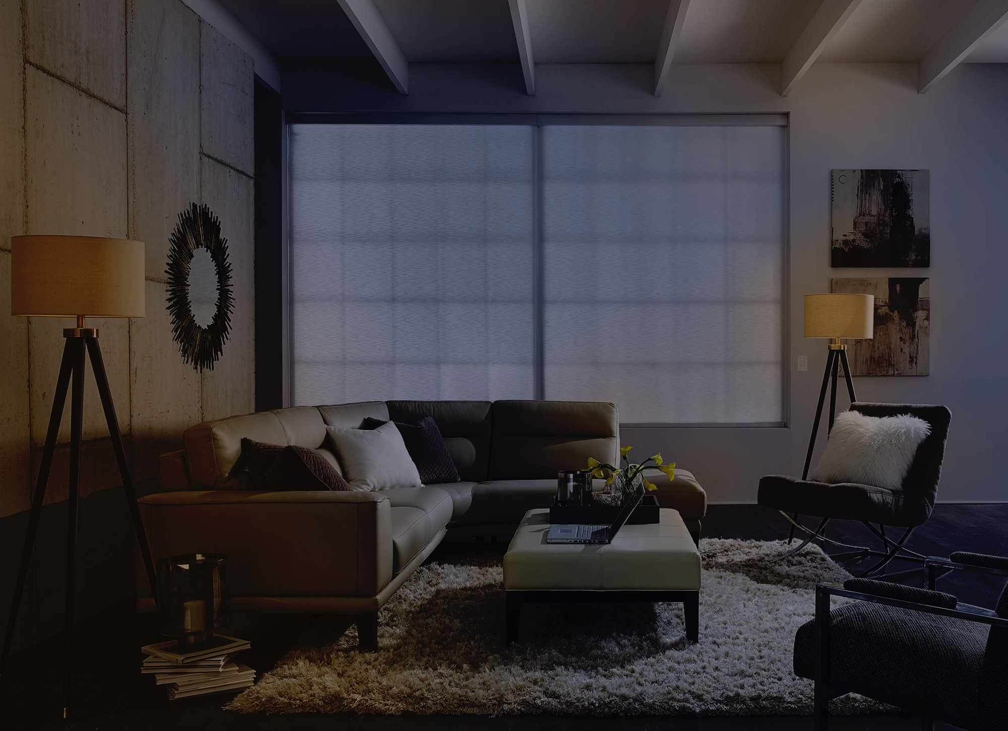 The living room at night: deep shadows fill the corners, the sofa and rug are dimly lit, and the roller shades are down, conveying a quiet, restful “bedtime” mood.
