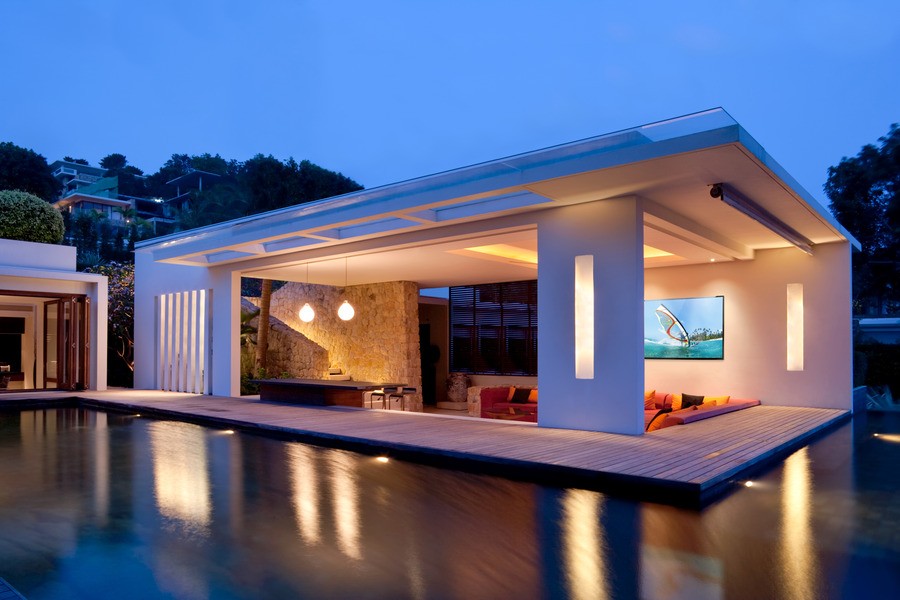 A backyard patio in the evening with an infinity pool and cove lighting.