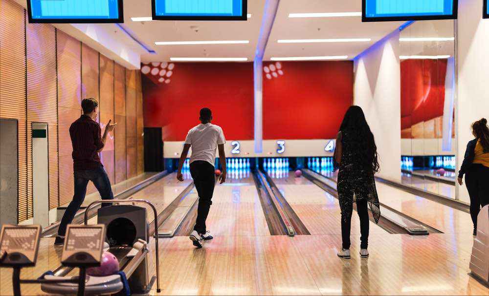 Several friends bowl together in a sleek bowling alley, one mid-throw while others watch the pins at the end of the lane.